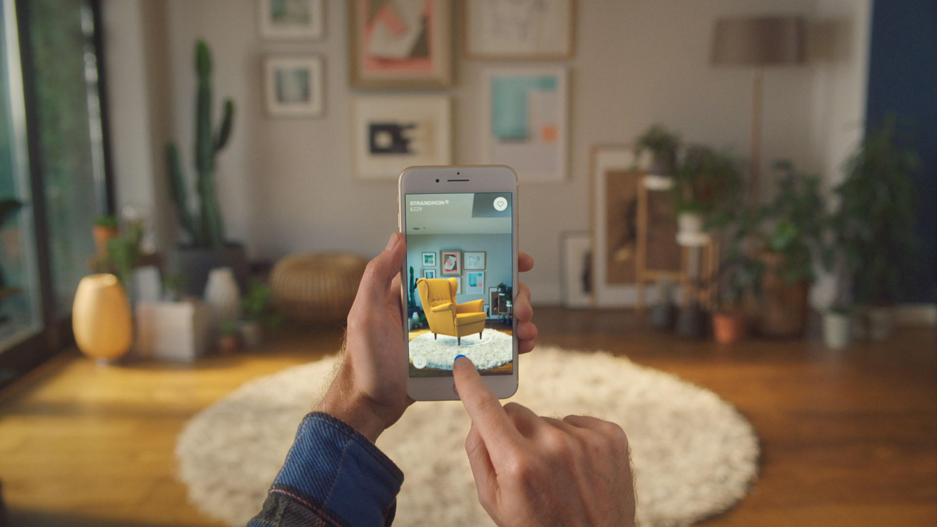 A smartphone held by its user. The screen captures the living room in the background with the addition of a lounge chair.